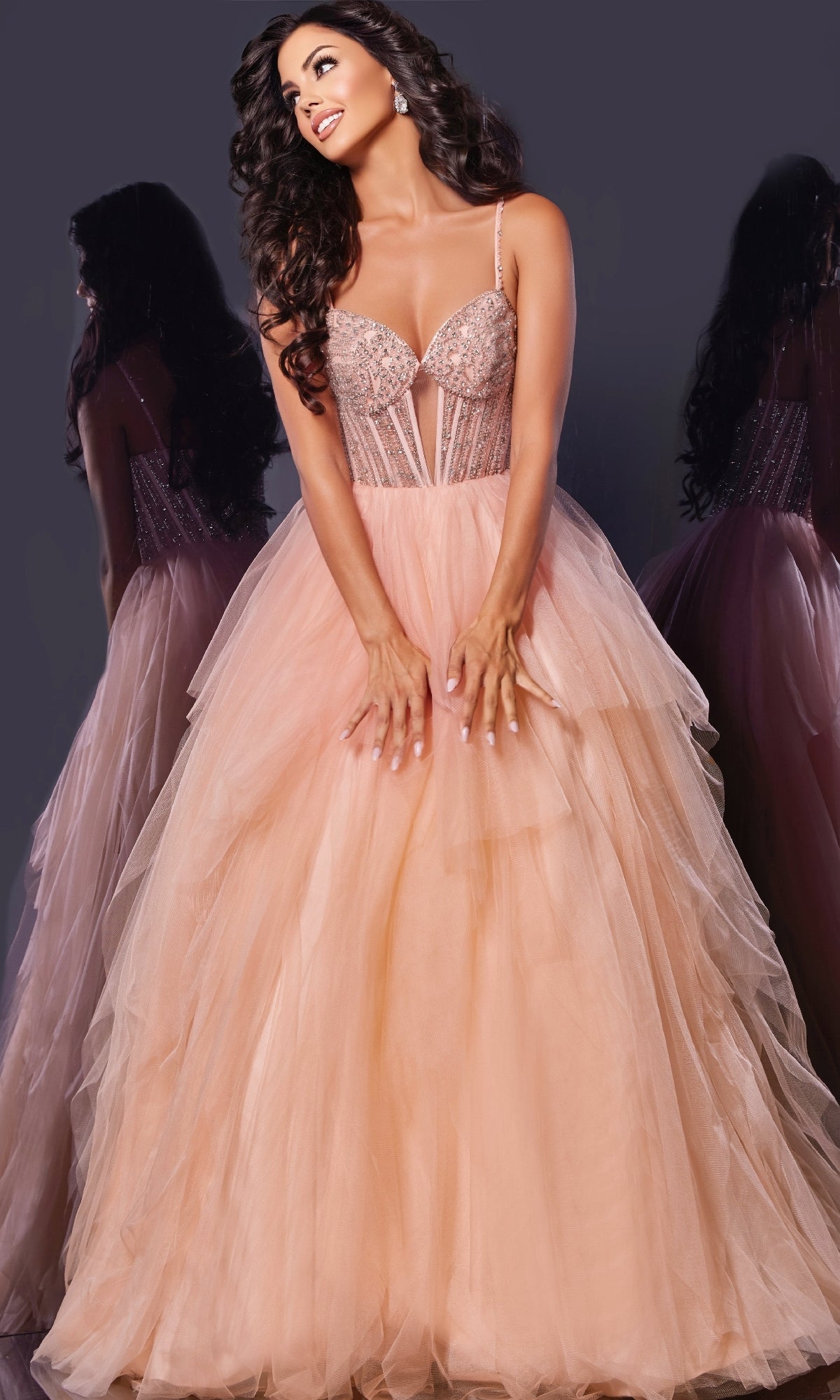 A woman poses in the Jovani 43254 long prom dress, featuring a blush pink hue, fitted embellished corset bodice, and layered tulle skirt; her reflection is seen on both sides against a dark background.